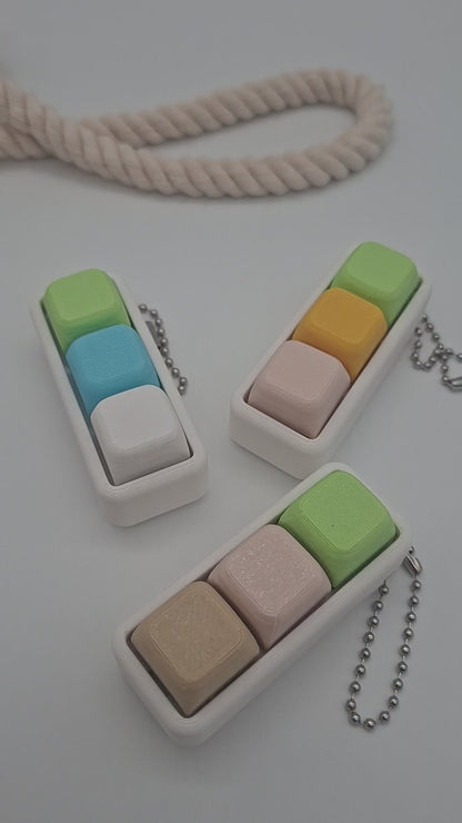 Pastellfarbener Keyboard Klicker mit drei Keycaps auf weißem Gehäuse als sensorisches Fidget für Konzentration und Entspannung.